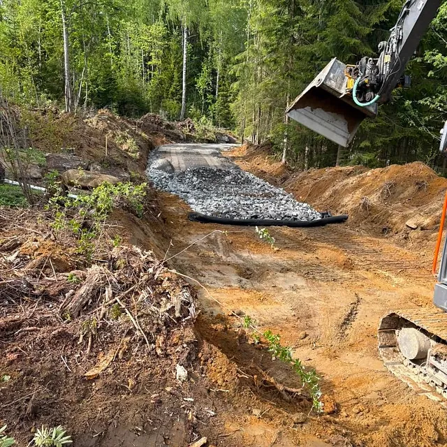 Gravemaskin graver grøft i skogsterreng